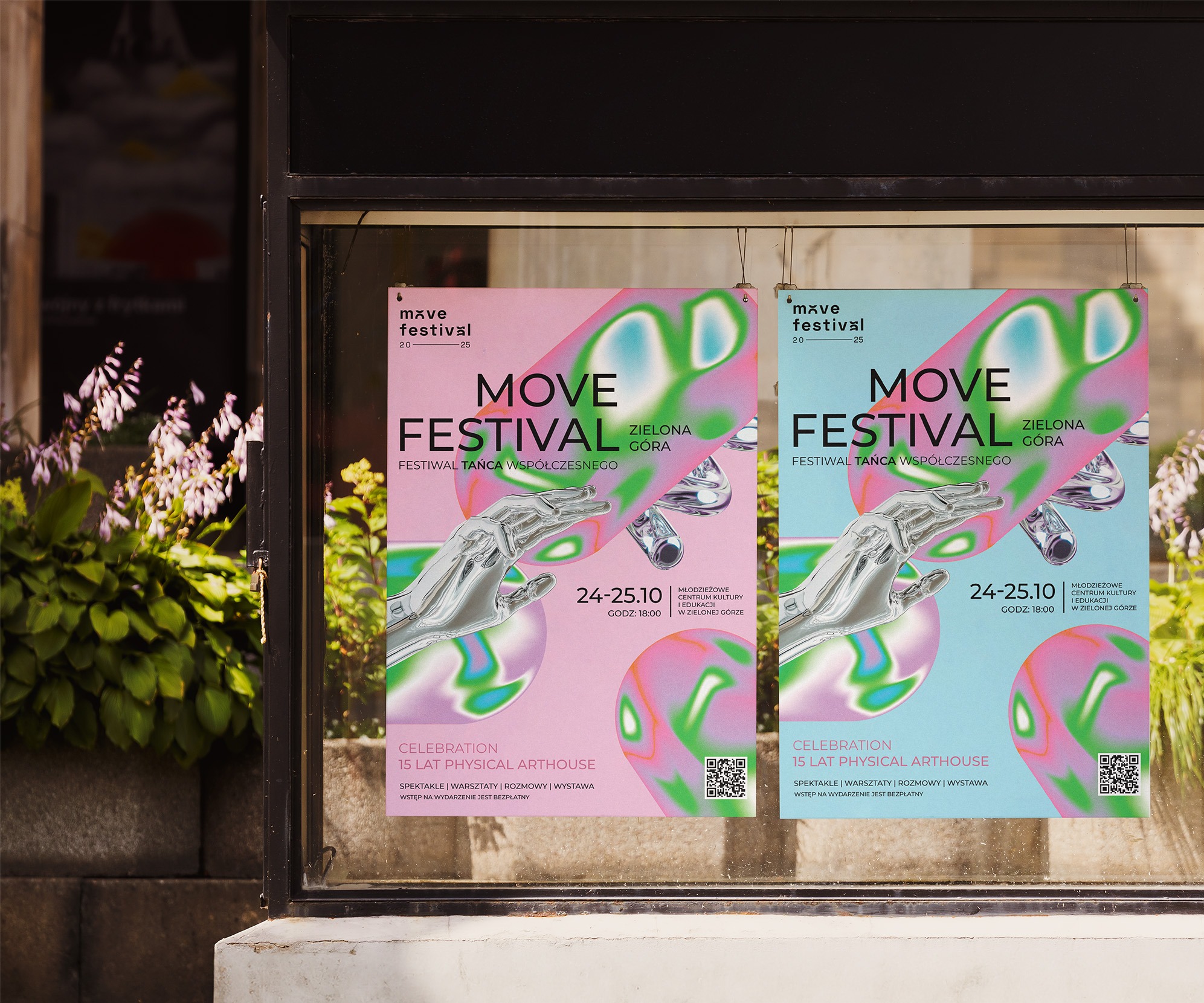 Dwa plakaty z grafiką i napisem 'Move Festival' w oknie wystawowym, z roślinami po lewej stronie. Plakaty w odcieniach różu i błękitu, informują o festiwalu tańca.