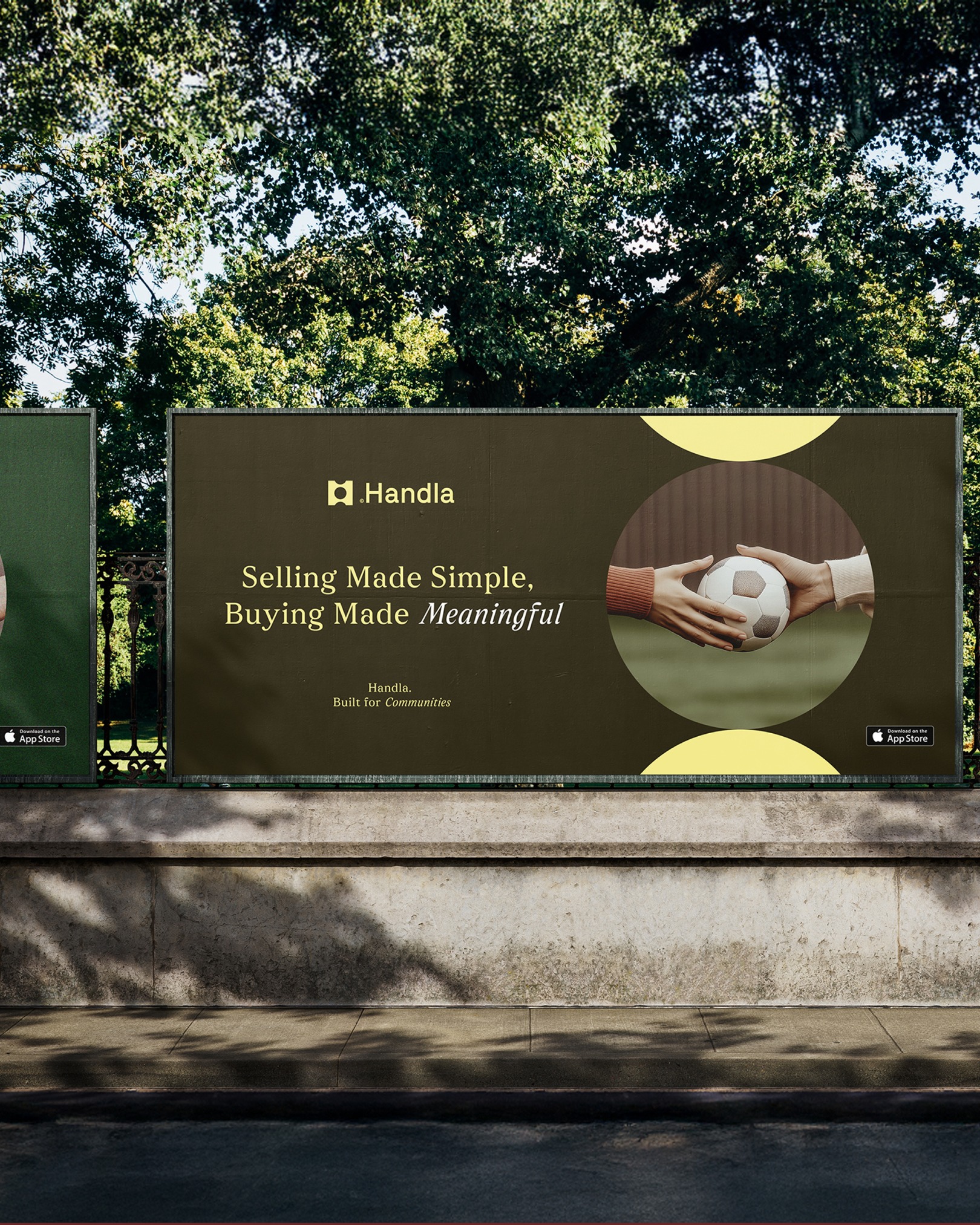 Billboard reklamowy Handla z hasłem 'Selling Made Simple, Buying Made Meaningful', na tle zieleni miejskiej. Dwie dłonie przekazują sobie piłkę. Widoczne logo i informacja o App Store.