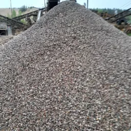 Góra żwiru pod taśmociągiem w kopalni, widoczne urządzenia do przesiewania i sortowania.