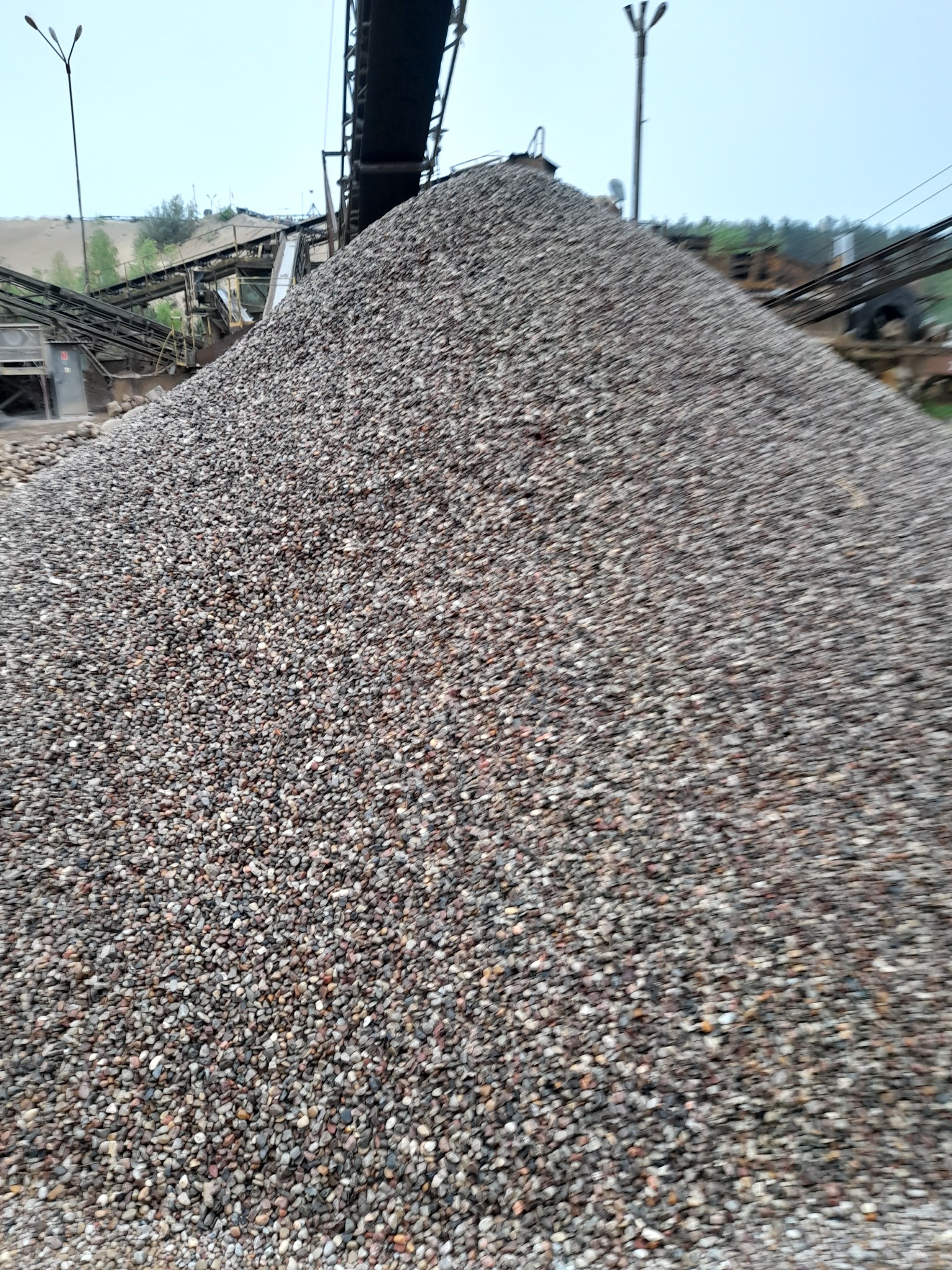 Góra żwiru pod taśmociągiem w kopalni, widoczne urządzenia do przesiewania i sortowania.