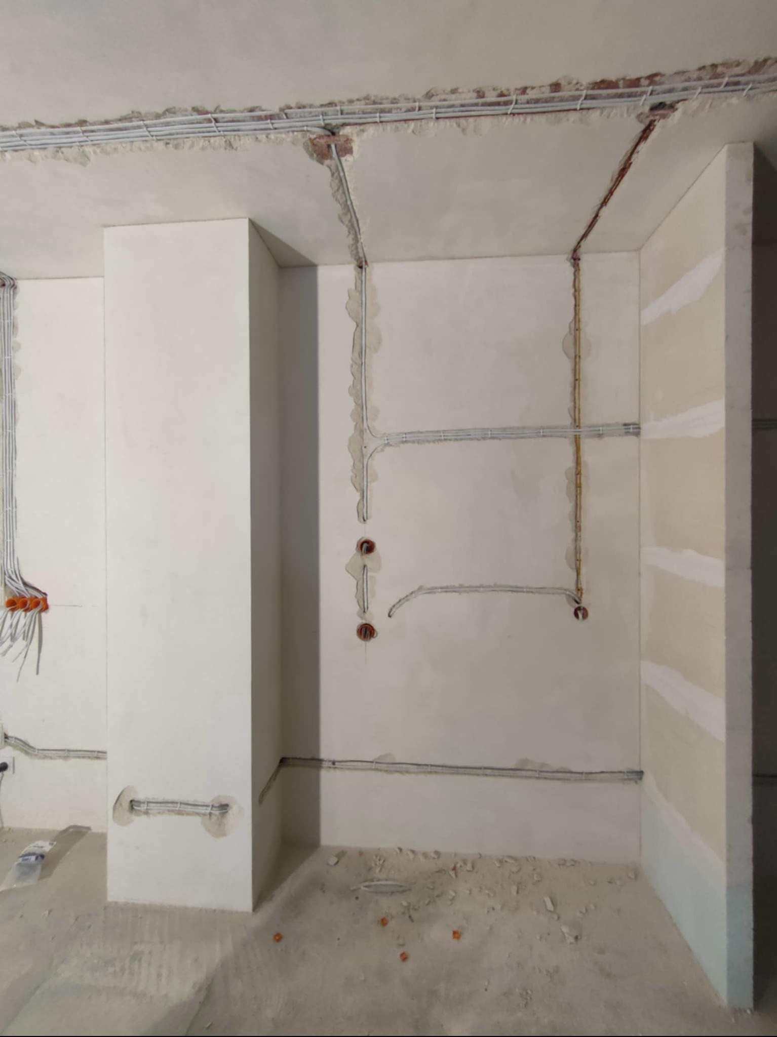 Wnętrze w trakcie prac elektrycznych: kable prowadzone po ścianach i suficie, widoczne puszki instalacyjne. Surowy stan wykończenia, ściany przygotowane do dalszych prac.