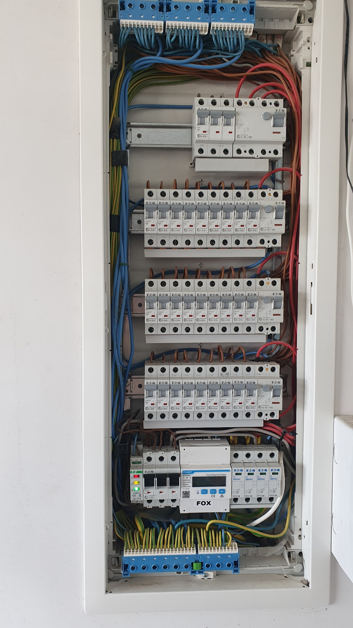 Rozdzielnica elektryczna z zamontowanymi bezpiecznikami, przewodami i licznikiem energii elektrycznej marki FOX. Widok na kompletną instalację wewnątrz skrzynki.