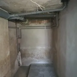 Szare rury PCV i miedziane rury grzewcze zamontowane pod betonowym sufitem w surowym, wilgotnym pomieszczeniu.