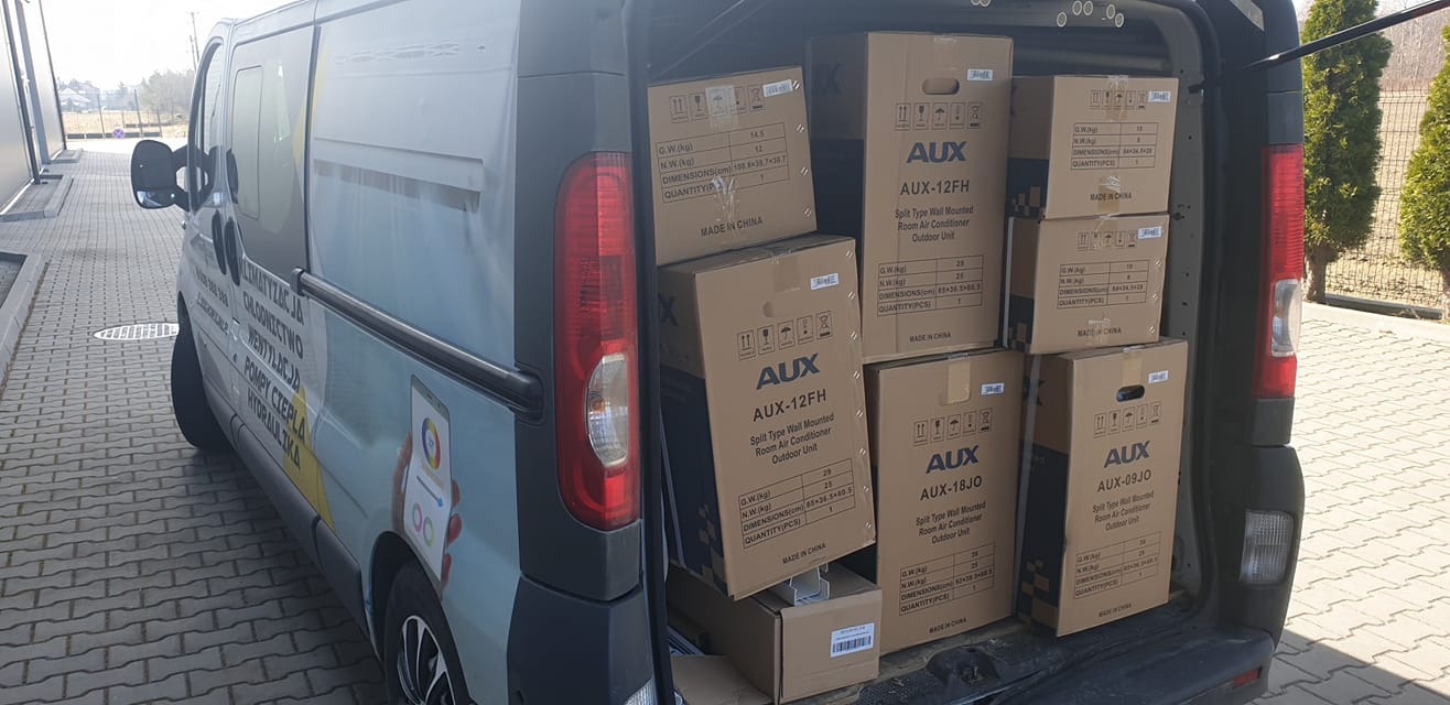 Van wypełniony kartonami klimatyzatorów AUX, widoczny bok pojazdu z reklamą usług klimatyzacji, wentylacji, pomp ciepła i hydrauliki.