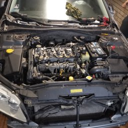 Samat Cars & Service - Otwarta maska samochodu z widocznym silnikiem w trakcie naprawy; narzędzia i ściereczka leżą na podszybiu, a przedni zderzak jest częściowo zdemontowany.