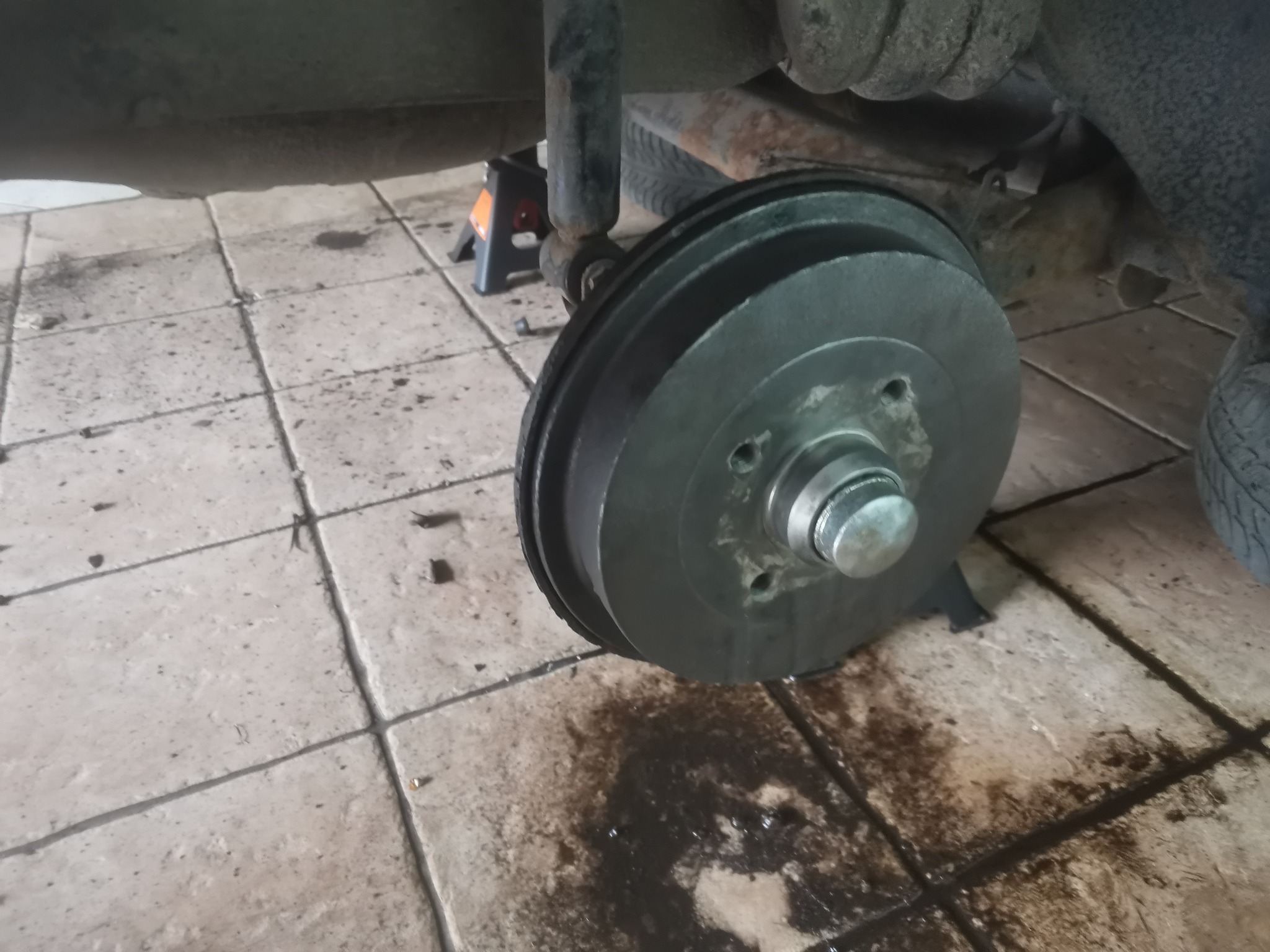 Odsłonięty bęben hamulcowy samochodu na podnośniku, widoczne ślady wycieku płynów eksploatacyjnych na podłodze warsztatu.