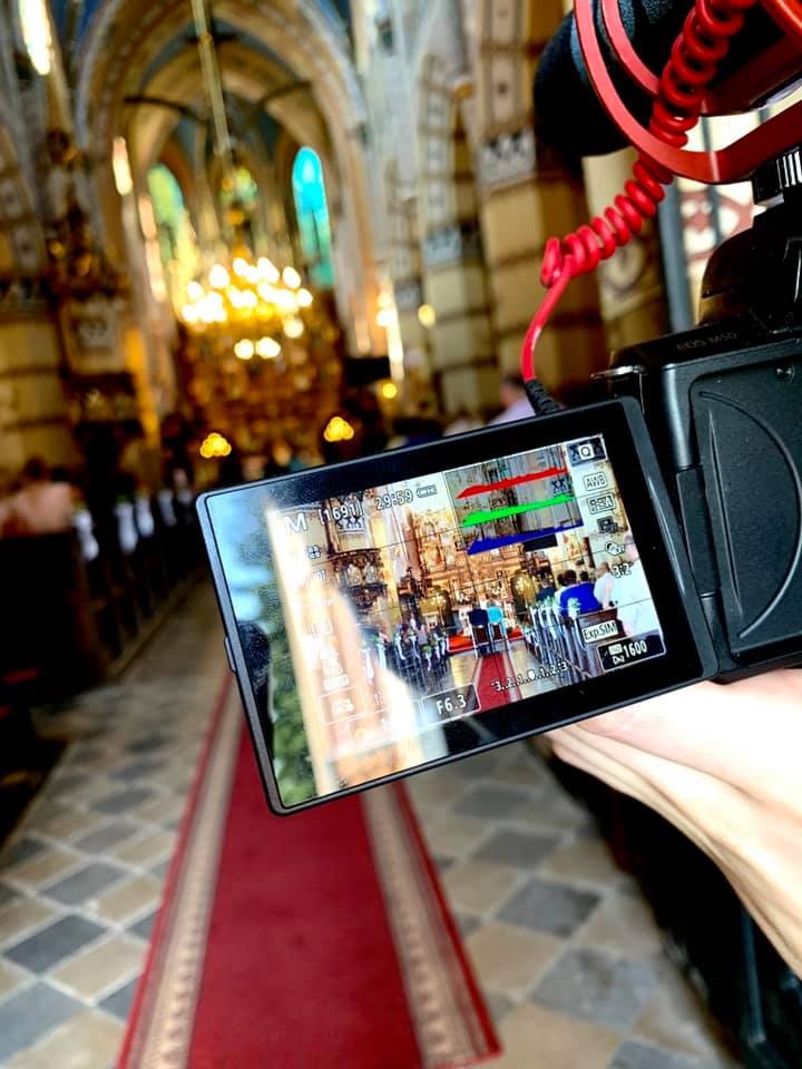 Kamera z widokiem na wnętrze kościoła, nagrywająca uroczystość, widoczna czerwona wykładzina i detale architektoniczne.