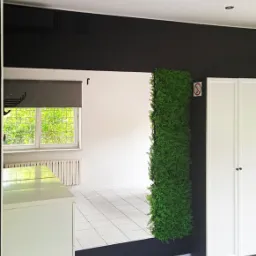 Wnętrze biura po remoncie, z czarnymi akcentami, białą szafą, sztuczną zieloną ścianą i nową podłogą z płytek.