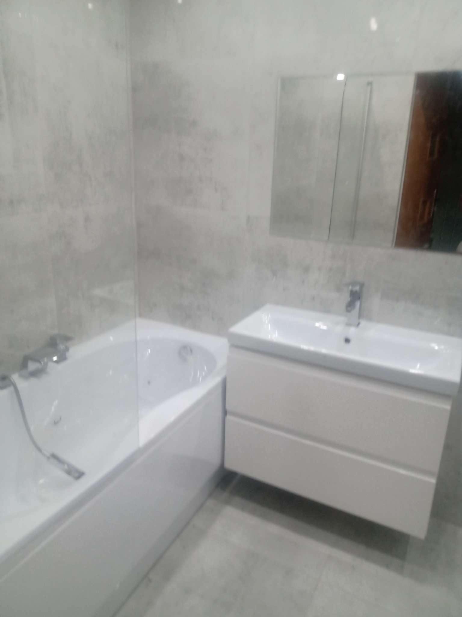 Nowoczesna łazienka w odcieniach szarości z białą wanną z parawanem nawannowym i szafką pod umywalką z lustrem.