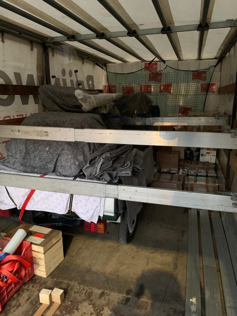 Wnętrze skrzyni ładunkowej pojazdu z ładunkiem zabezpieczonym kocami i siatką, widoczne półki z ładunkiem i elementy wyposażenia transportowego.