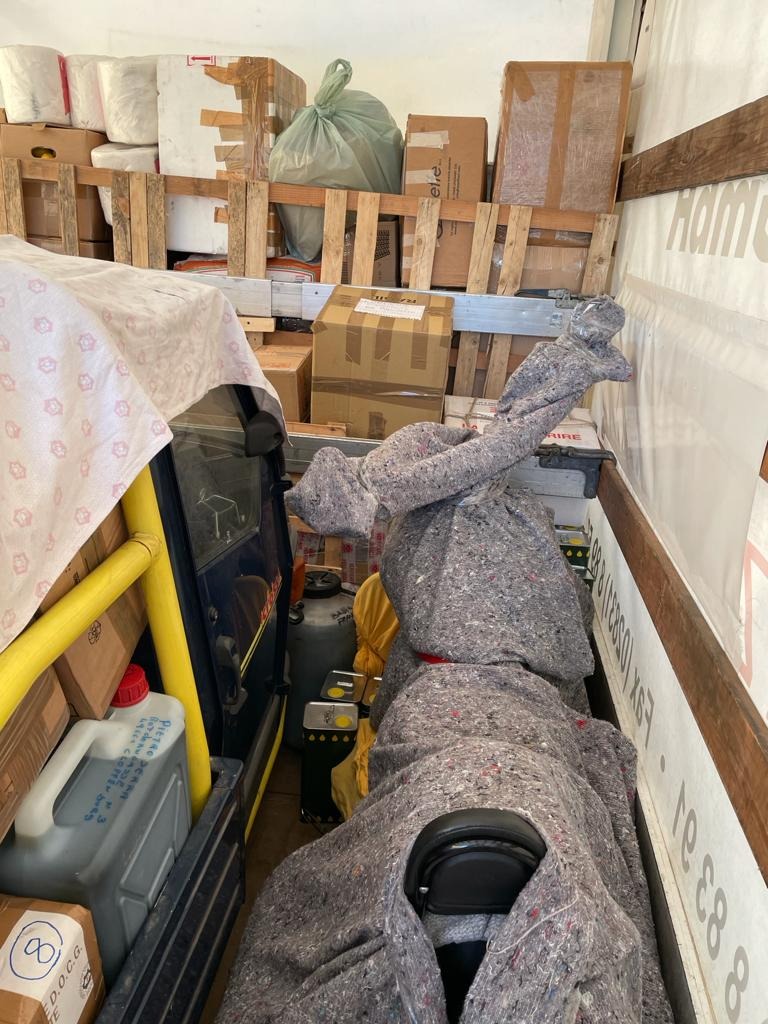 Wnętrze furgonetki załadowane kartonami, workami i meblami zabezpieczonymi szarym materiałem ochronnym, widoczne kanistry i butla z gazem.