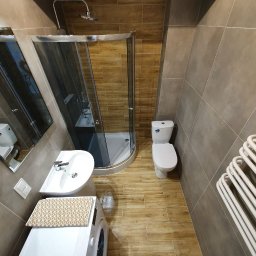 Wykończenia Marcin Kieryk Działalność usługowa - Nowoczesna łazienka z kabiną prysznicową, umywalką nablatową, toaletą i grzejnikiem drabinkowym, wykończona płytkami w odcieniach brązu i beżu, z drewnopodobną podłogą i pralką pod umywalką...