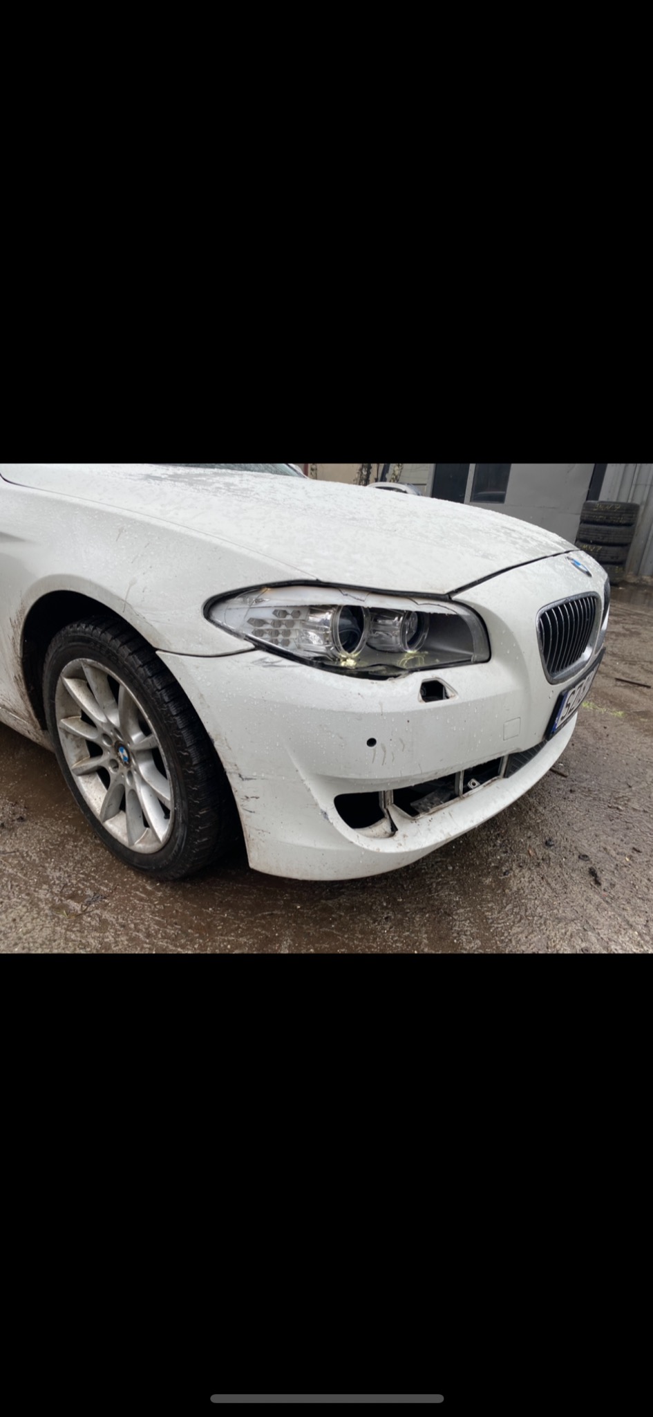 Uszkodzony przedni zderzak i reflektor białego BMW serii 5, widoczne ślady błota i uszkodzenia lakieru.