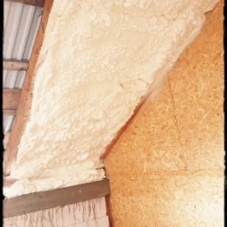 Poddasze ocieplone pianką PUR, widoczne drewniane krokwie, płyta OSB na ścianie szczytowej oraz białe worki z wełną mineralną w dolnej części zdjęcia.