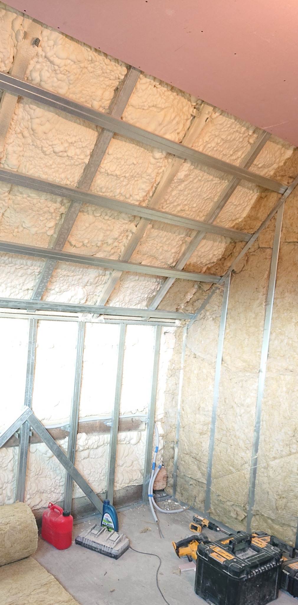 Sromowce Wyżne: Wnętrze poddasza w trakcie prac, widoczne metalowe profile konstrukcyjne, częściowo wypełnione pianką izolacyjną, z fragmentami nieocieplonej ściany i narzędziami na podłodze.