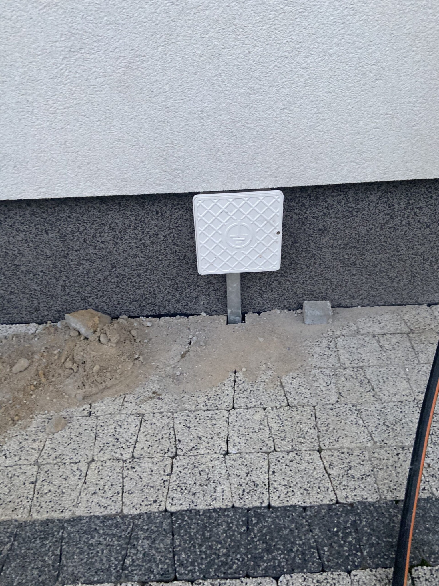 Uziemienie instalacji elektrycznej przy budynku w Krośnie, zabezpieczone białą skrzynką z symbolem uziemienia, zamontowane na szarej rurze.