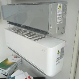 Dwa klimatyzatory ścienne: szary model Elis u góry i biały model Teta Series poniżej, oba zamontowane na białej ścianie. Pod spodem leżą broszury reklamowe.