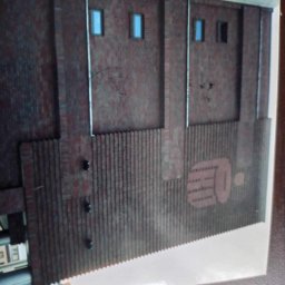 Klinkierek - Ceglana elewacja budynku z małymi oknami i dekoracyjnym elementem z pionowych żeberek oraz wzorem graficznym w kolorze cegły, sfotografowana pod kątem.