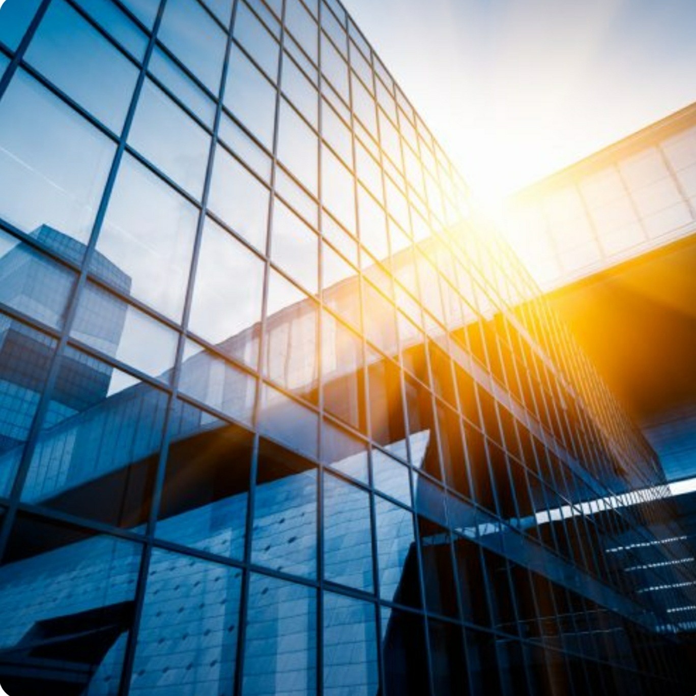 Nowoczesny budynek biurowy z fasadą ze szkła refleksyjnego, widziany pod kątem, z silnym blaskiem słońca odbijającym się od szyb.