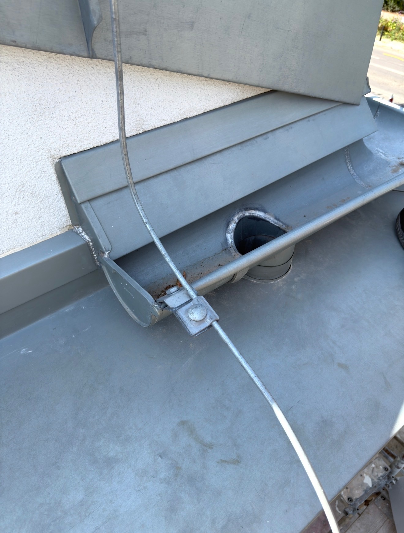 Szary dach z metalową rynną, widoczne mocowanie odgromowe i spawane łączenia blacharskie. Detal konstrukcyjny dachu z bliska.