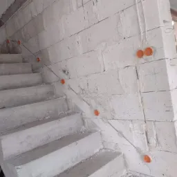 Surowe schody betonowe w trakcie budowy, z widocznymi pomarańczowymi puszkami instalacyjnymi i przewodami elektrycznymi w ścianie z białych bloczków.