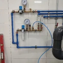 Kompleksowy system rur wodnych i gazowych z manometrami i filtrami, zamontowany na kafelkowanej ścianie, widoczny poziomica z boku.