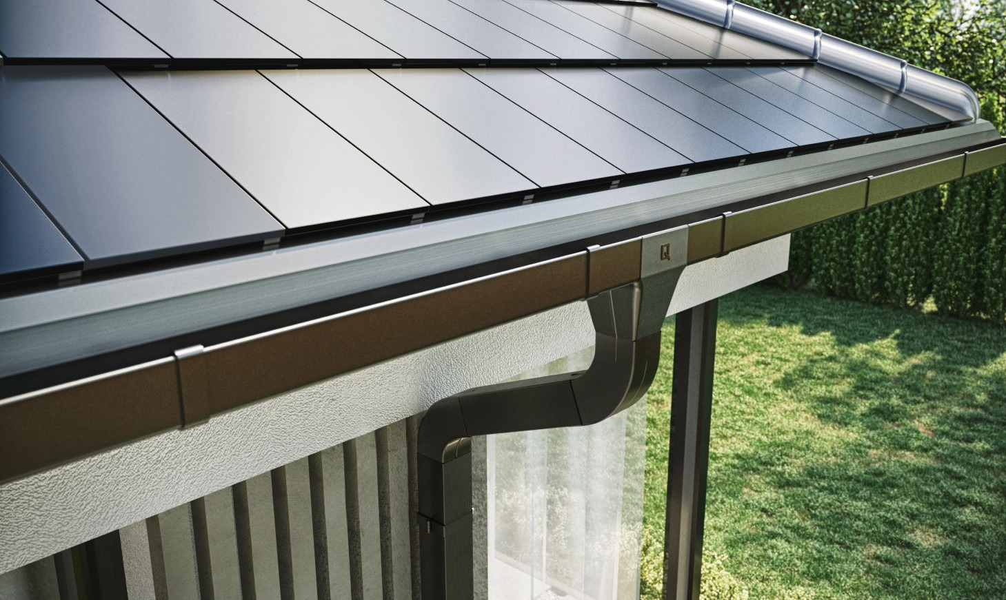 Nowoczesny system rynnowy w kolorze grafitowym, zamontowany na dachu z płaskiej dachówki, widok z dołu na tle zielonego trawnika.