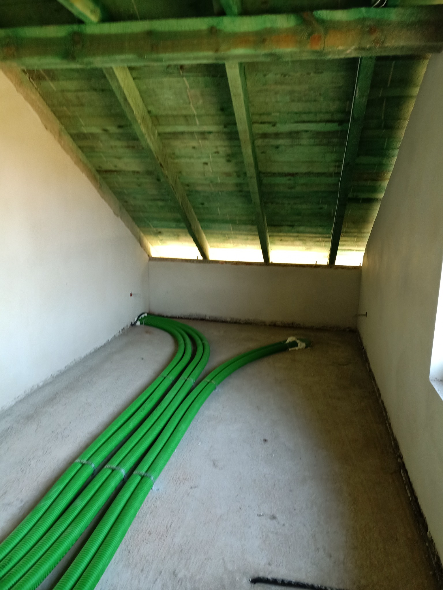Zielone rury wentylacyjne prowadzone po podłodze poddasza z drewnianą konstrukcją stropu.