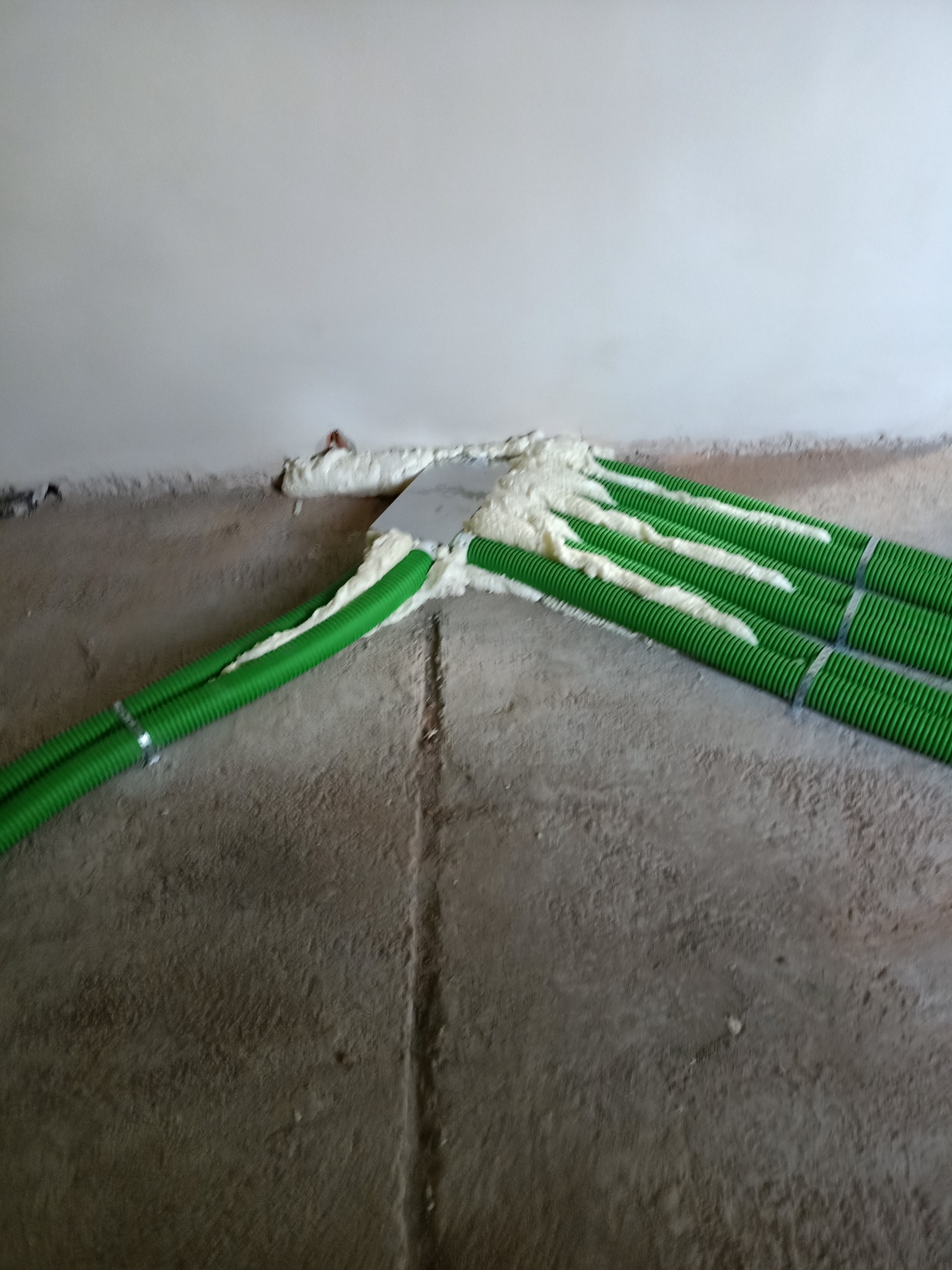 Montaż zielonych, karbowanych rur wentylacyjnych, uszczelnionych pianką montażową przy ścianie w surowym wnętrzu.