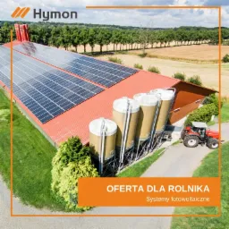 Farma z czerwonym dachem i panelami fotowoltaicznymi, silosami oraz traktorem, otoczona zielenią i polami, z widocznym logo firmy Hymon.
