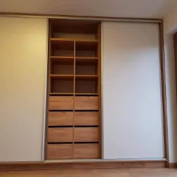 Wnętrze szafy przesuwnej z jasnymi frontami, drewnianymi półkami i szufladami, widok z boku na okno.