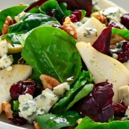 Sałatka z serem, gruszką, karmelizowanymi orzechami włoskimi, suszoną żurawiną, podana na szpinaku