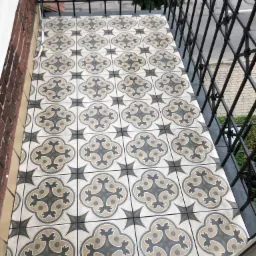 Wyłożony wzorzystymi płytkami balkon z czarną, metalową balustradą, widok z góry.