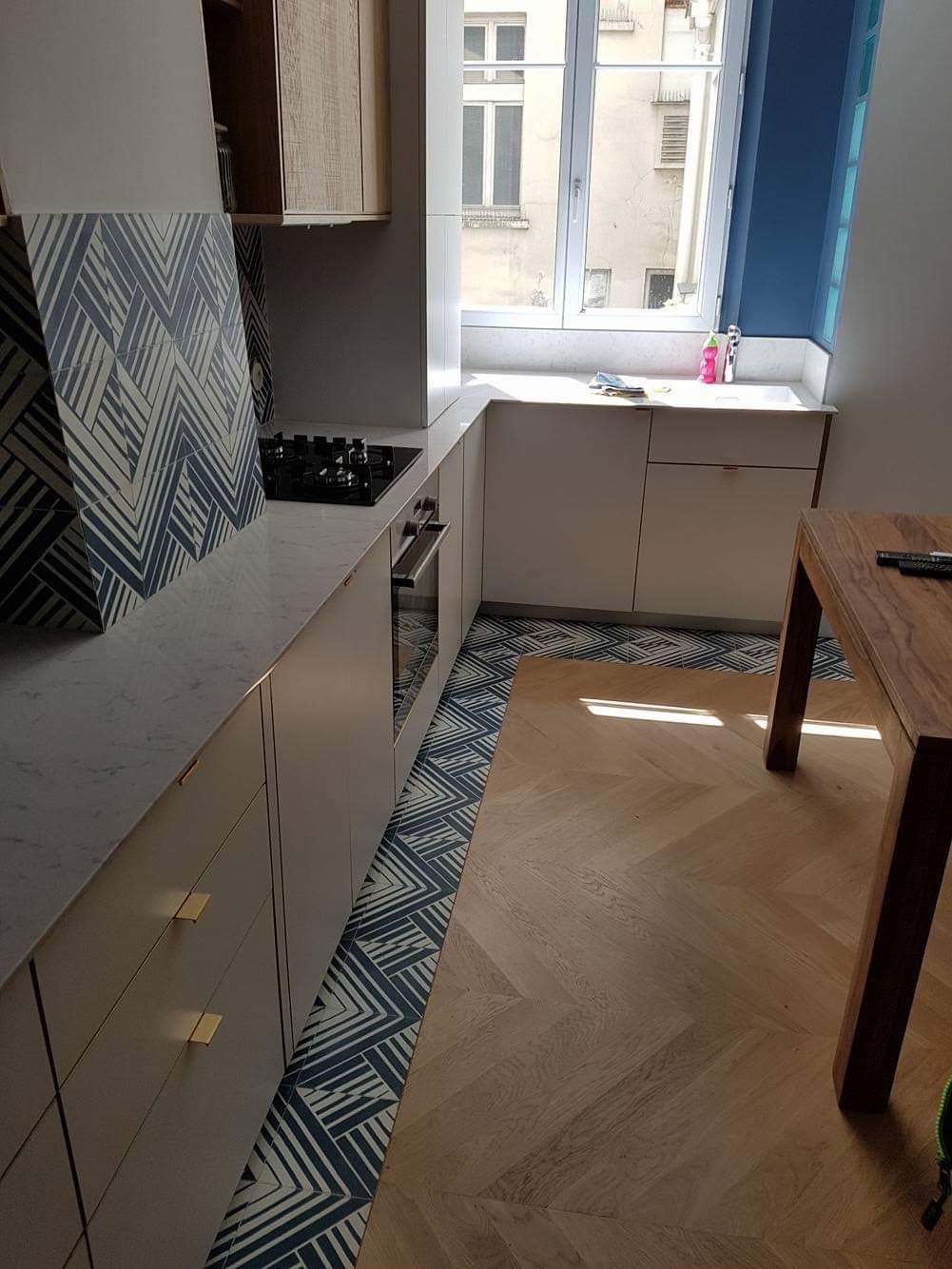 Wykończona kuchnia w Krosno z drewnianą podłogą w jodełkę i płytkami z geometrycznym wzorem, widoczne szafki kuchenne i blat z kuchenką.