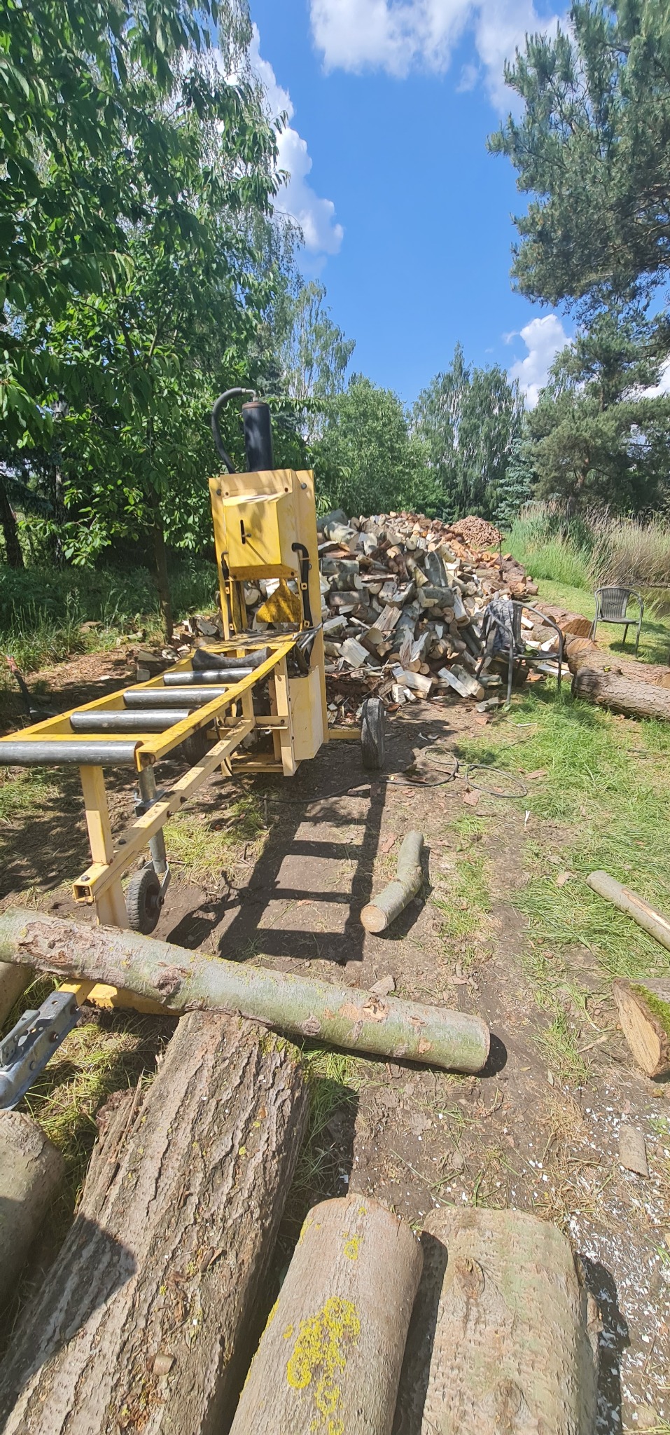 Żółta maszyna do cięcia drewna, ułożone pocięte drewno w tle, Nadarzyn.
