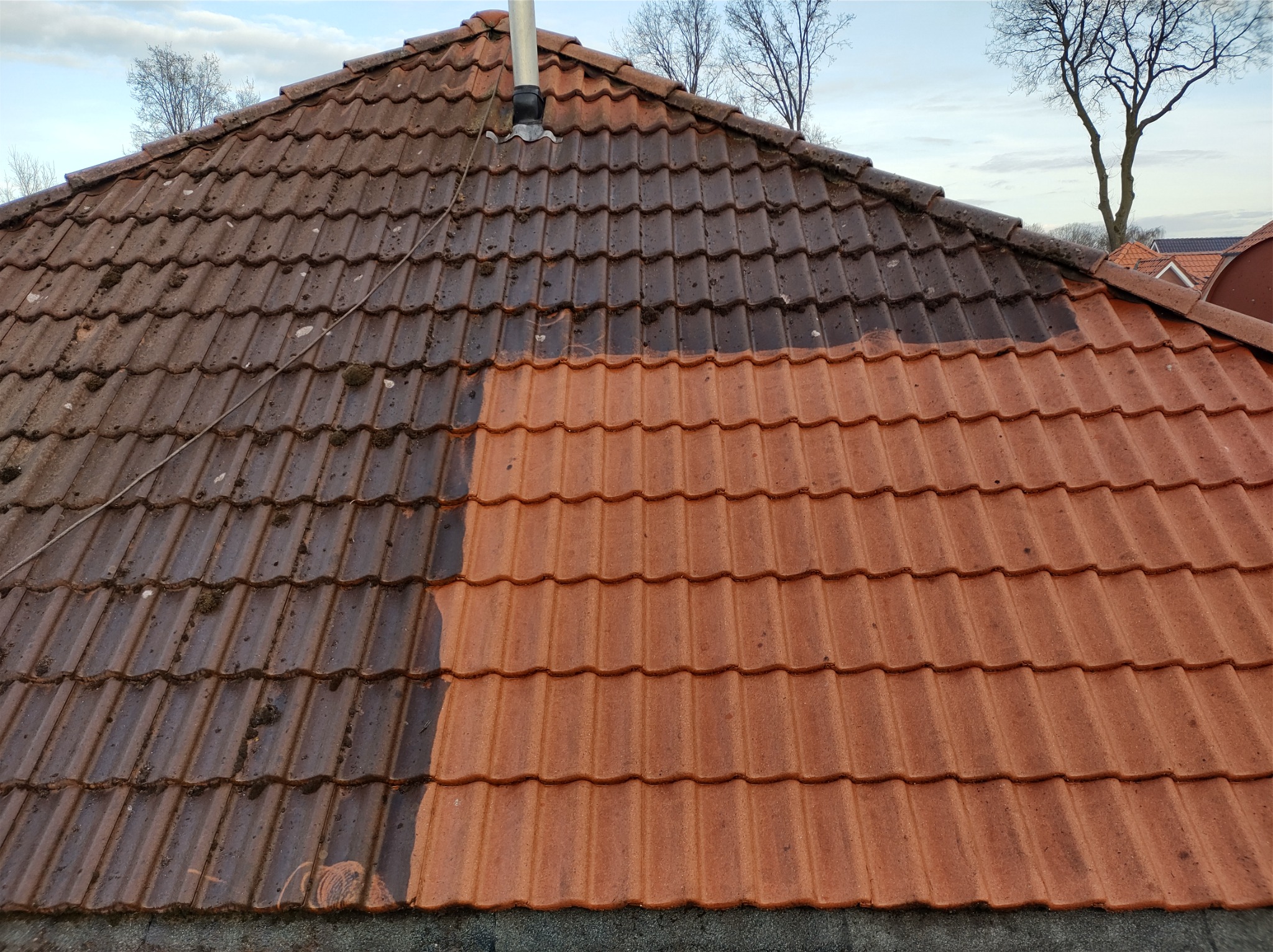 Częściowo oczyszczony dach z dachówki ceramicznej, widoczna wyraźna różnica między brudną i czystą powierzchnią, komin na dachu.