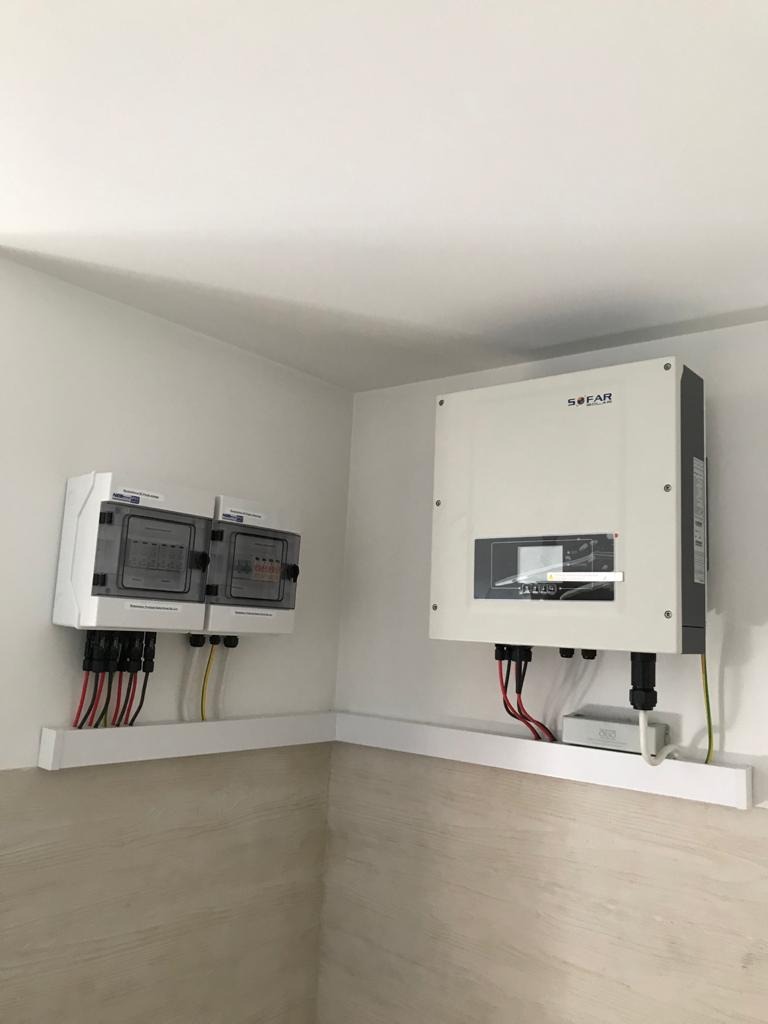 Biały inwerter Sofar i dwie skrzynki zabezpieczeń DC z okablowaniem na tle jasnej ściany i drewnopodobnej boazerii.