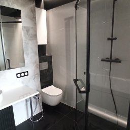 PRO-FLIZ - Nowoczesna łazienka z czarną armaturą, szarymi płytkami imitującymi marmur, czarną podłogą z połyskiem i kabiną prysznicową typu walk-in z czarnymi profilami.