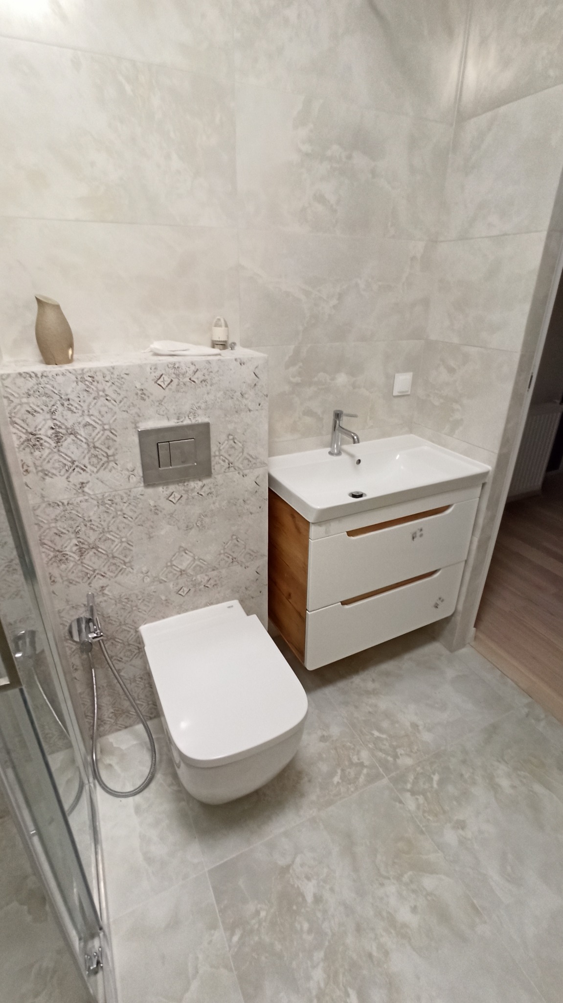 Wykończona łazienka we Wrocławiu z podwieszaną toaletą, umywalką z szafką z drewnianymi akcentami i beżowymi płytkami imitującymi marmur na ścianach i podłodze.