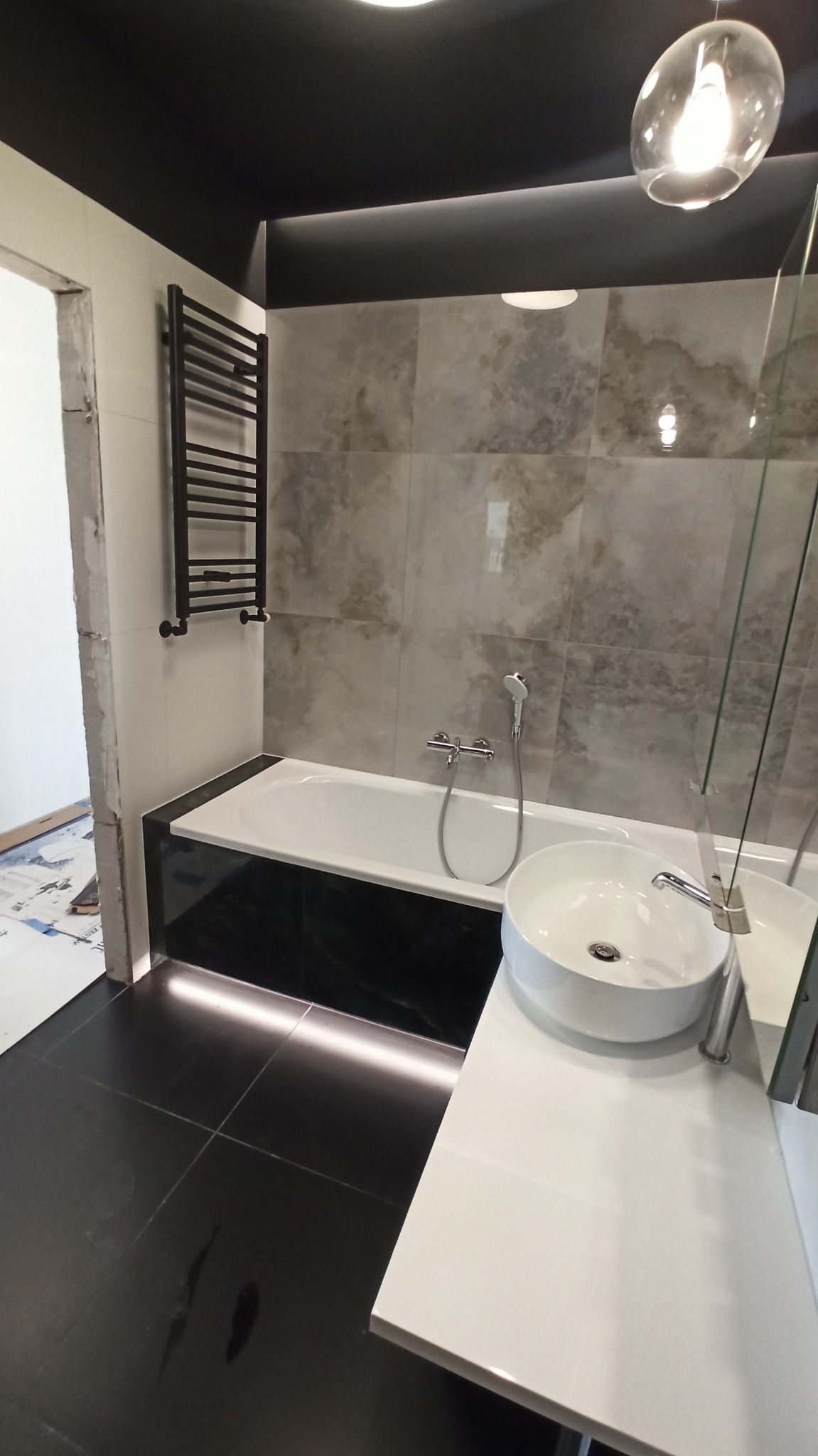 Nowoczesna łazienka z czarną armaturą, płytkami imitującymi marmur i podświetleniem LED pod wanną, widoczny fragment niezakończonego remontu.