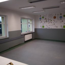 Usługi Instalacyjno-Remontowe Wojciech Struski - Pomalowane ściany w sali lekcyjnej z motywami chemicznymi, widoczne okna i grzejniki, szare panele ścienne, jasne oświetlenie sufitowe.