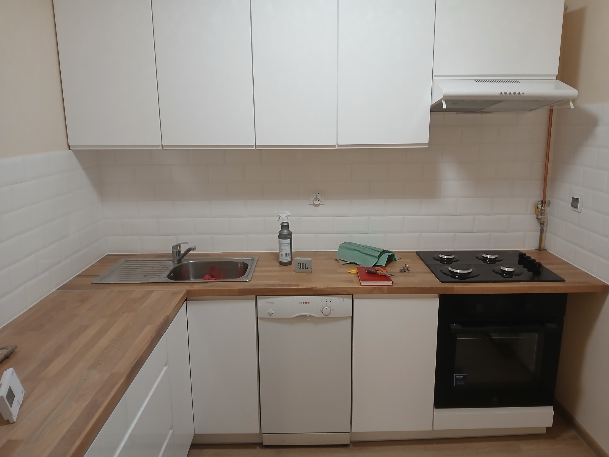 Wnętrze kuchni po remoncie: białe szafki, drewniany blat, białe płytki na ścianie, zamontowana płyta gazowa i piekarnik, widoczne ślady po pracy, butelka ze środkiem czyszczącym, głośnik JBL...