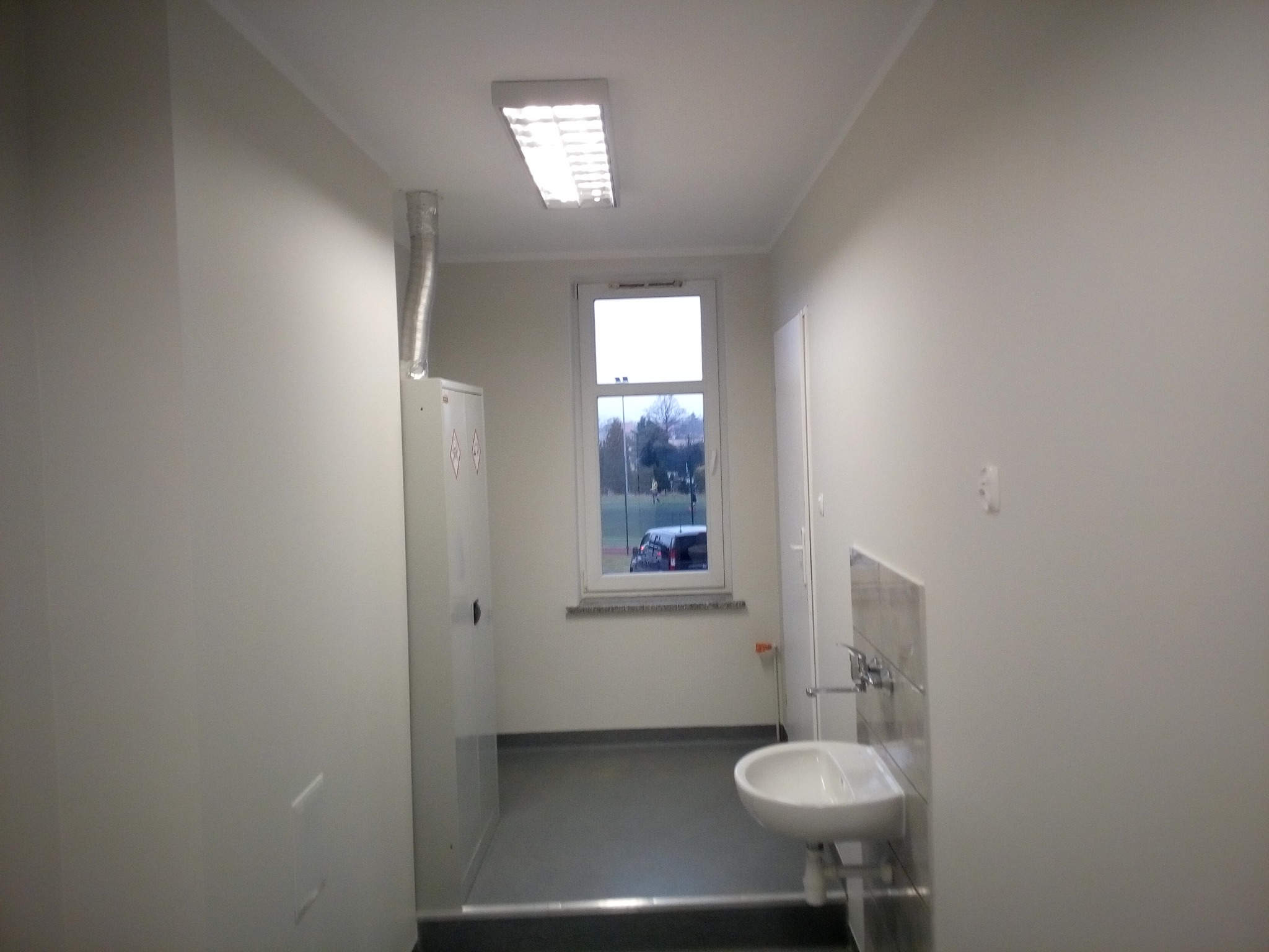 Wnętrze łazienki po remoncie, widoczna umywalka, białe ściany i szafka z wentylacją, okno z widokiem na zewnątrz.