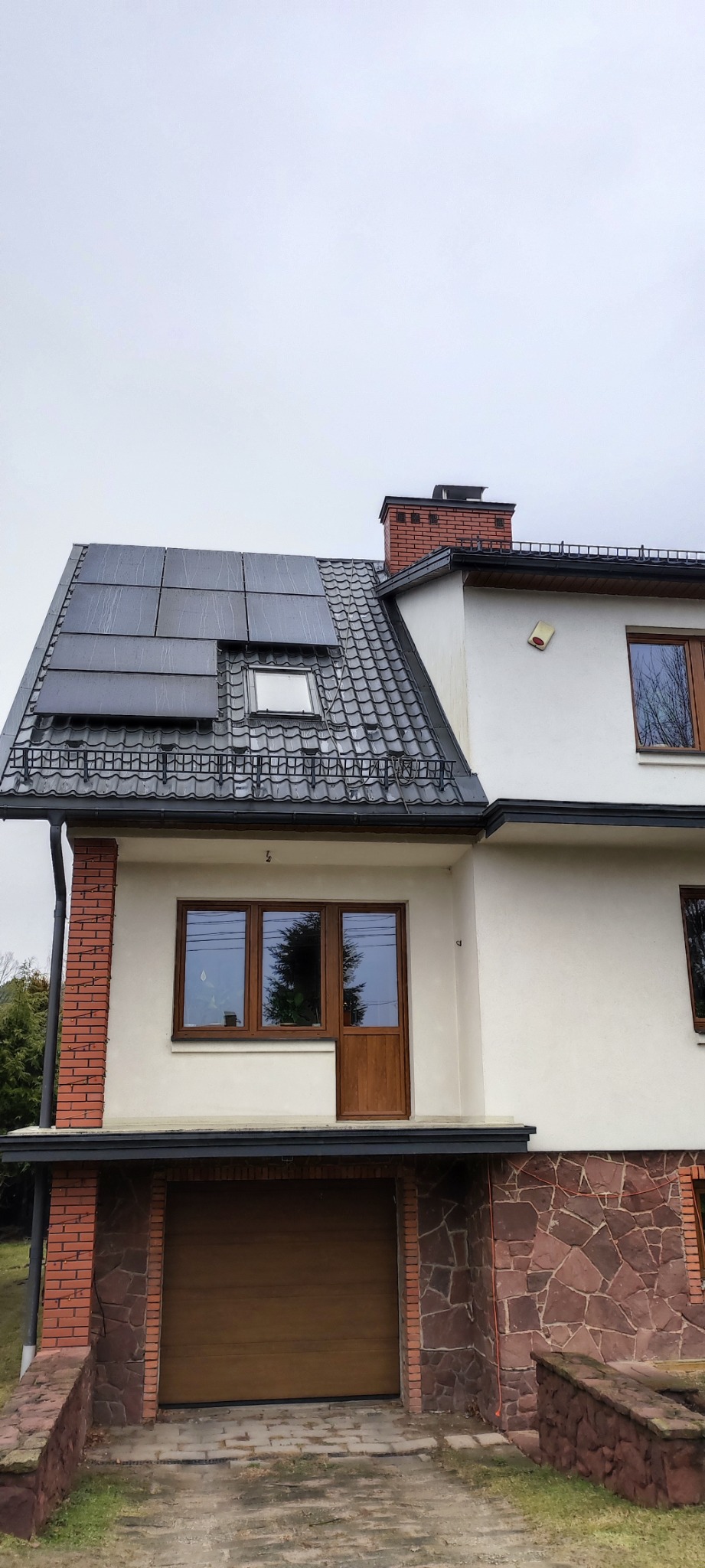 Dom jednorodzinny z panelami słonecznymi na dachu pokrytym dachówką, widoczny komin z cegły i okna z brązowymi ramami