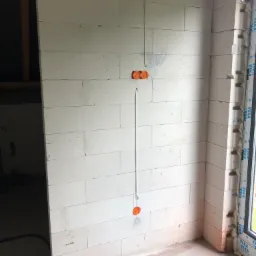 Wewnętrzna ściana z betonu komórkowego w surowym stanie, z widocznymi puszkami elektrycznymi i przewodami w bruzdach, przygotowana pod tynk.