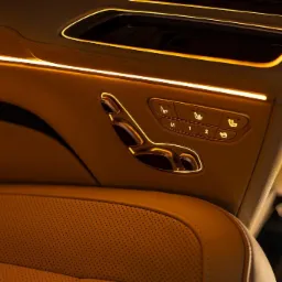 Wnętrze luksusowego samochodu z beżową, perforowaną skórzaną tapicerką, podświetlanymi elementami i panelami sterowania fotelami z zapamiętanymi ustawieniami.