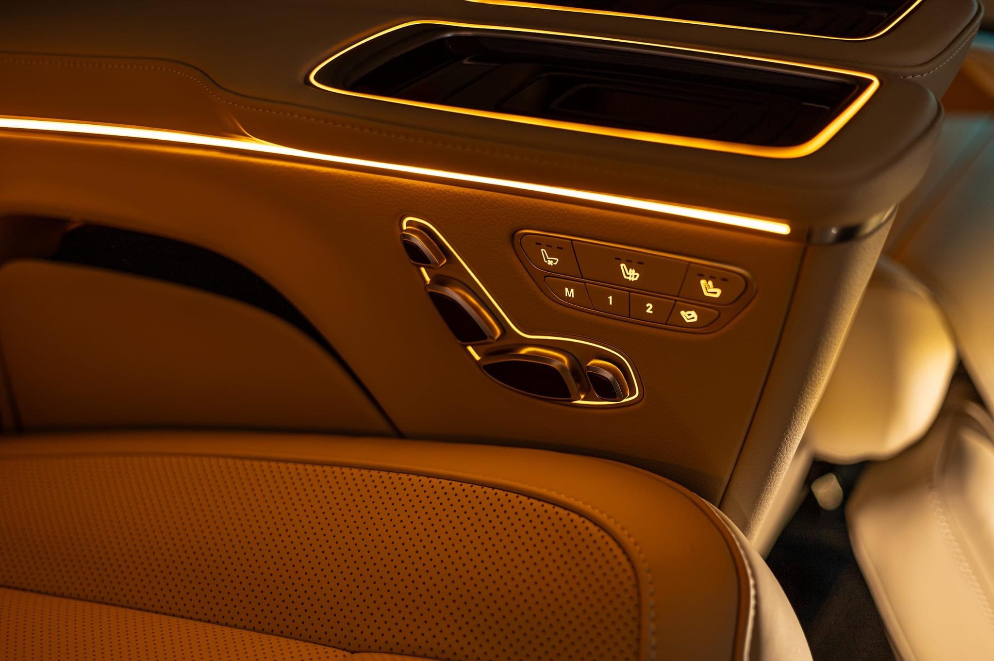 Wnętrze luksusowego samochodu z beżową, perforowaną skórzaną tapicerką, podświetlanymi elementami i panelami sterowania fotelami z zapamiętanymi ustawieniami.