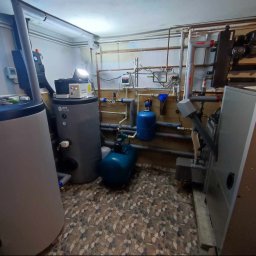 Passive Instal Sp. z o.o.- Mateusz Sztacherski - Zestaw zbiorników akumulacyjnych w kotłowni z licznymi rurami, zaworami i manometrami, z widocznym logo OEM Solar na jednym ze zbiorników.