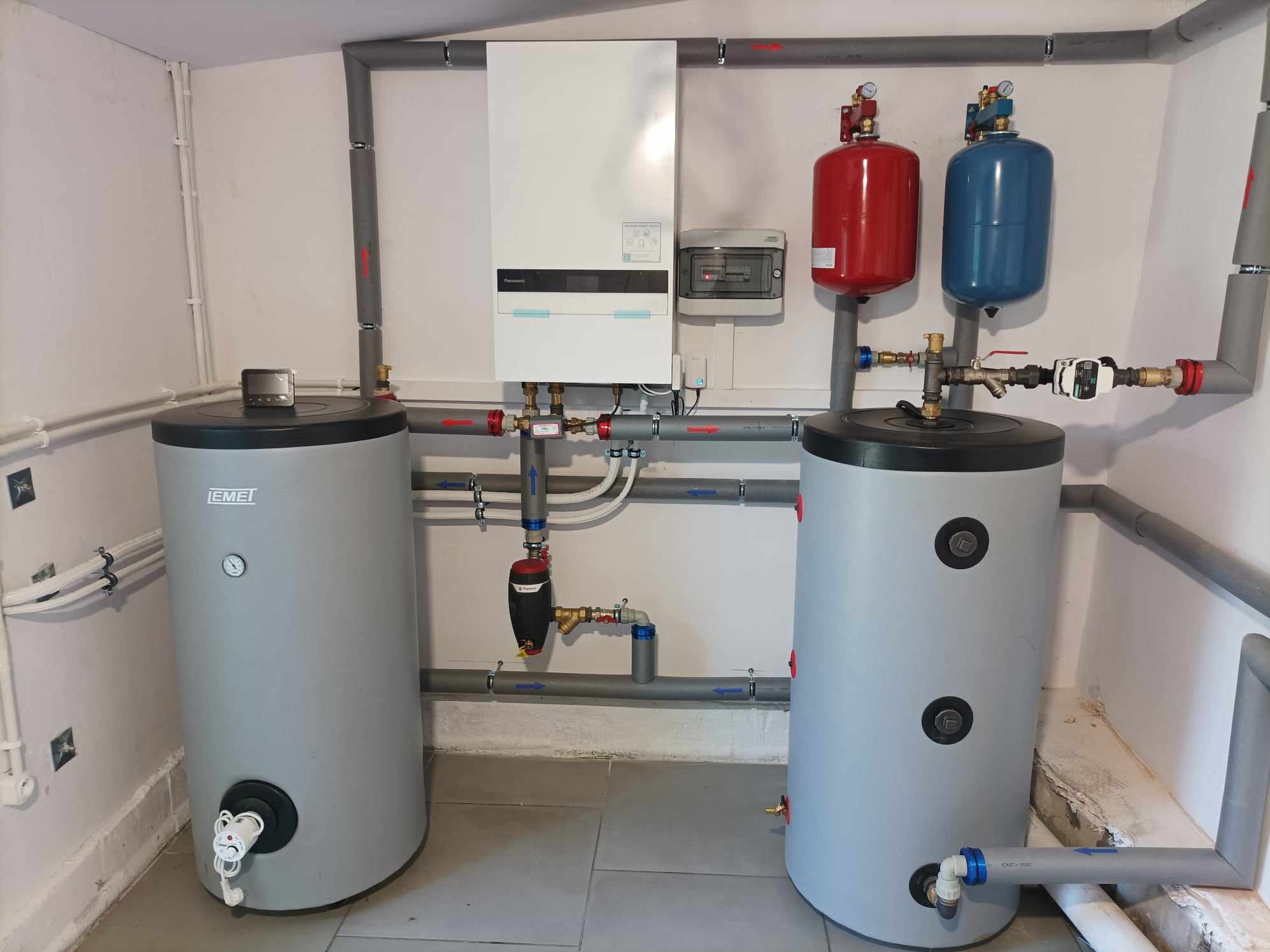 Kompletna instalacja centralnego ogrzewania z dwoma szarymi zbiornikami EMEI, białym piecem Panasonic, czerwonym i niebieskim zbiornikiem wyrównawczym, oraz szarymi rurami w kotłowni w Częstochowie.