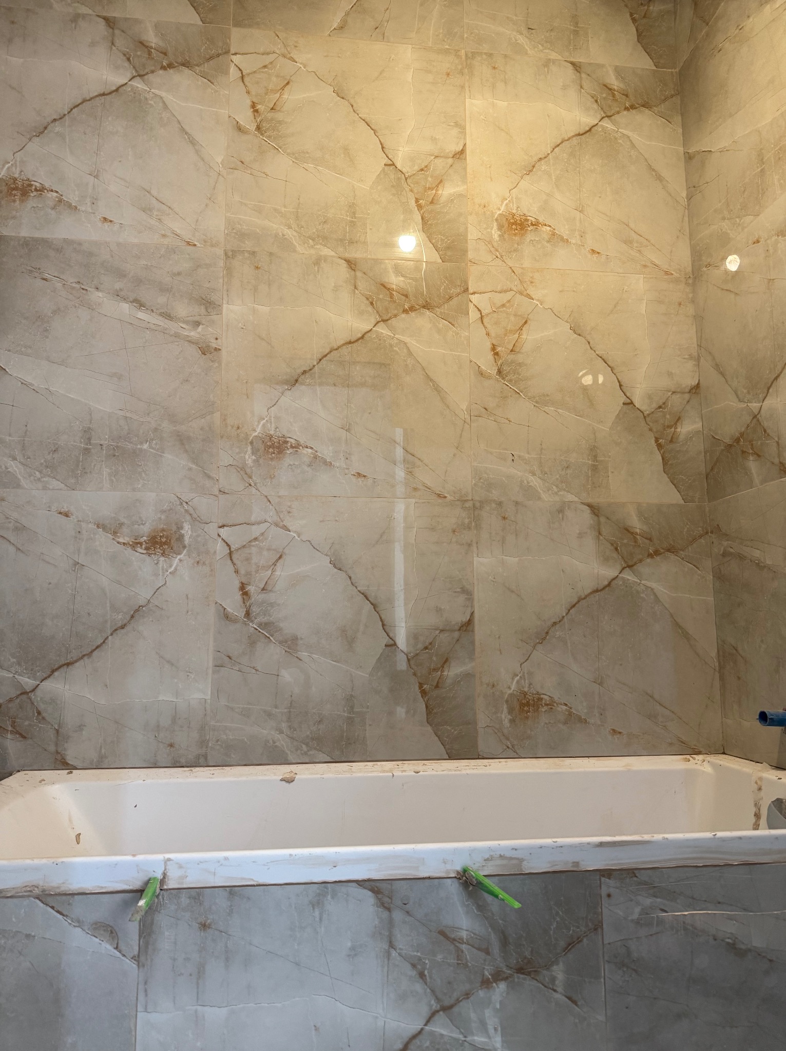 Wykończona ściana łazienki z marmurowymi płytkami w odcieniach beżu i brązu, z widoczną białą wanną. Detale wykończeniowe.